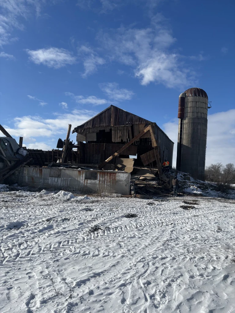 Old barn taken down beside a concrete silo in winter