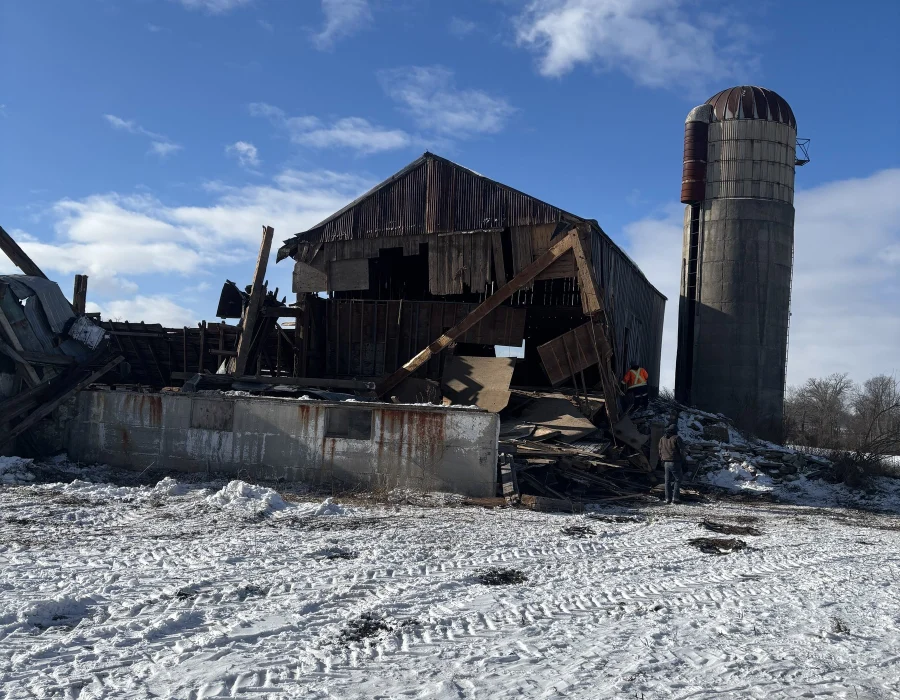 Old barn taken down beside a concrete silo in winter