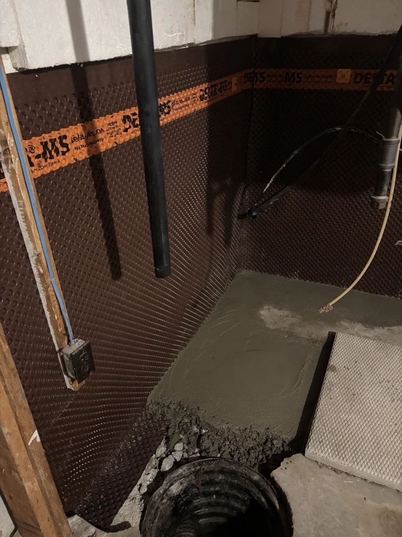 Dimpled waterproofing membrane on basement walls beside a new concrete patch
