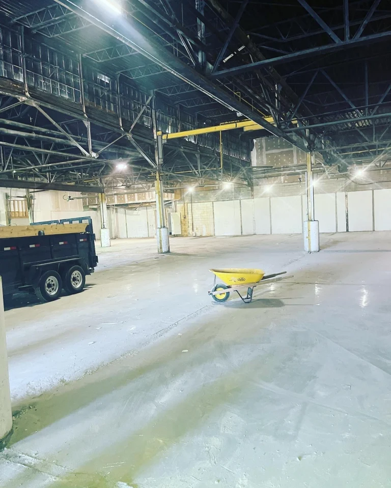 Large warehouse floor cleared, with a dump trailer and wheelbarrow inside