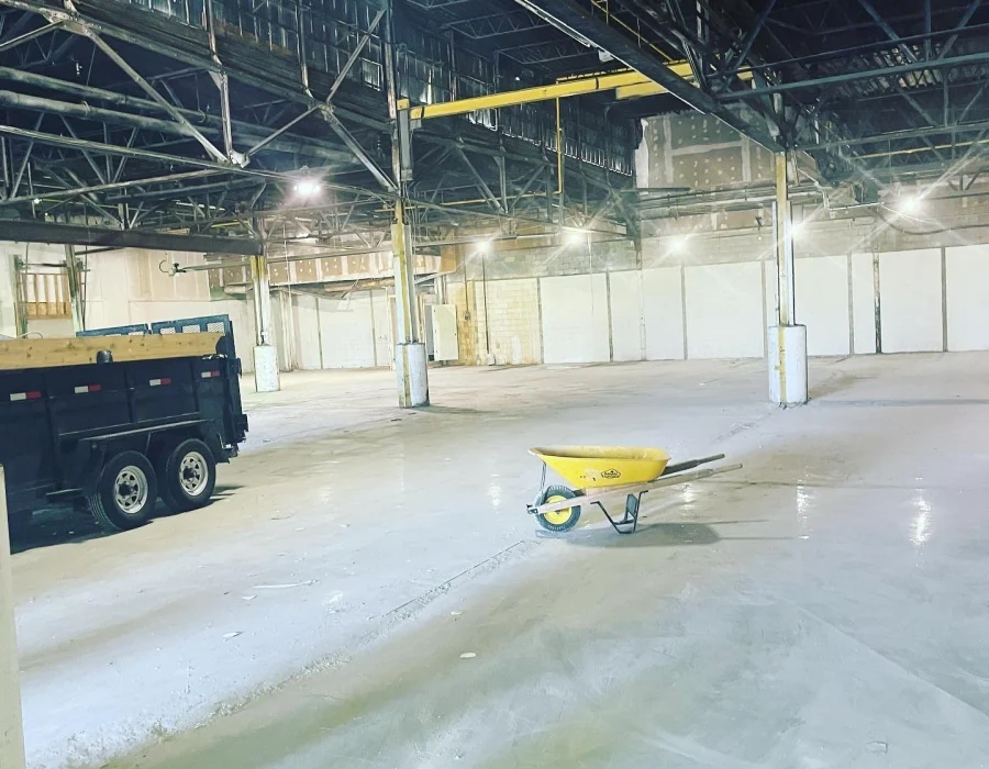 Large warehouse floor cleared, with a dump trailer and wheelbarrow inside